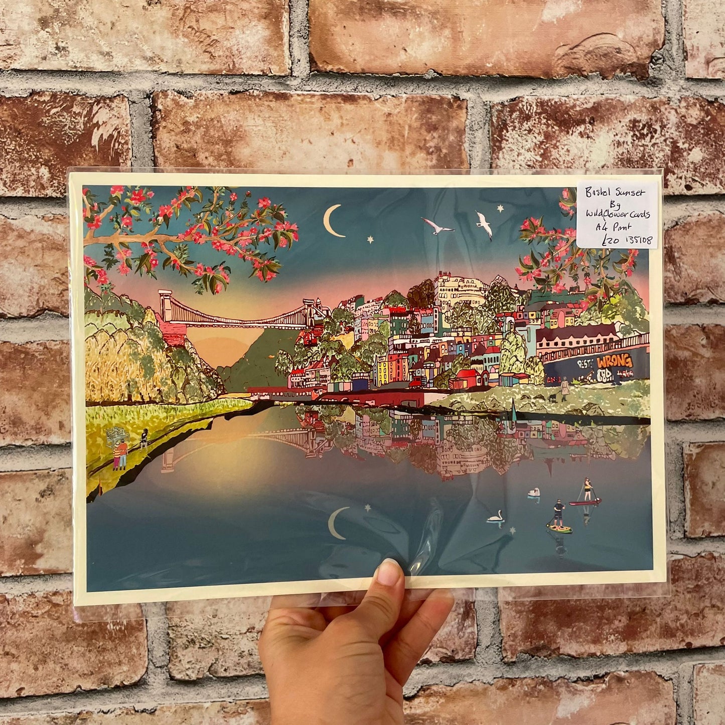 Illustrated poster of a cityscape with a bridge held against a brick wall.
