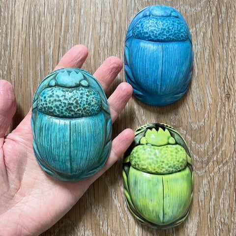 Three colorful scarab beetles on a wooden surface with a hand holding one.