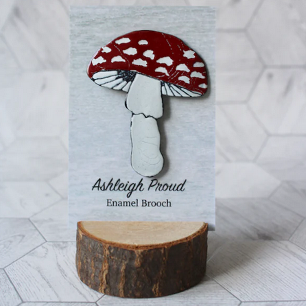 Mushroom-shaped enamel brooch on a wooden stand with a white background