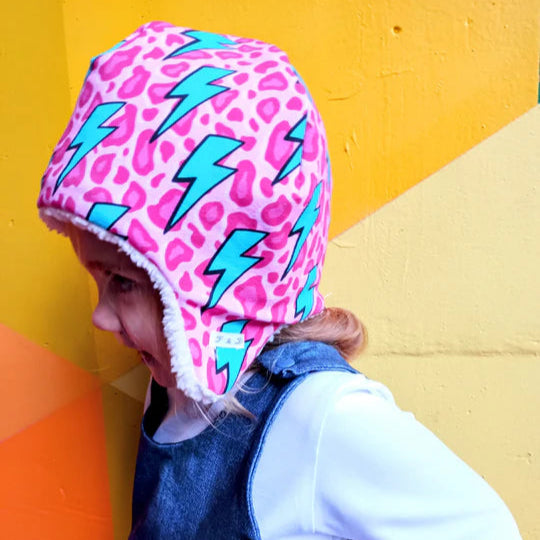 Child wearing a pink helmet with blue lightning bolts against a colorful geometric background