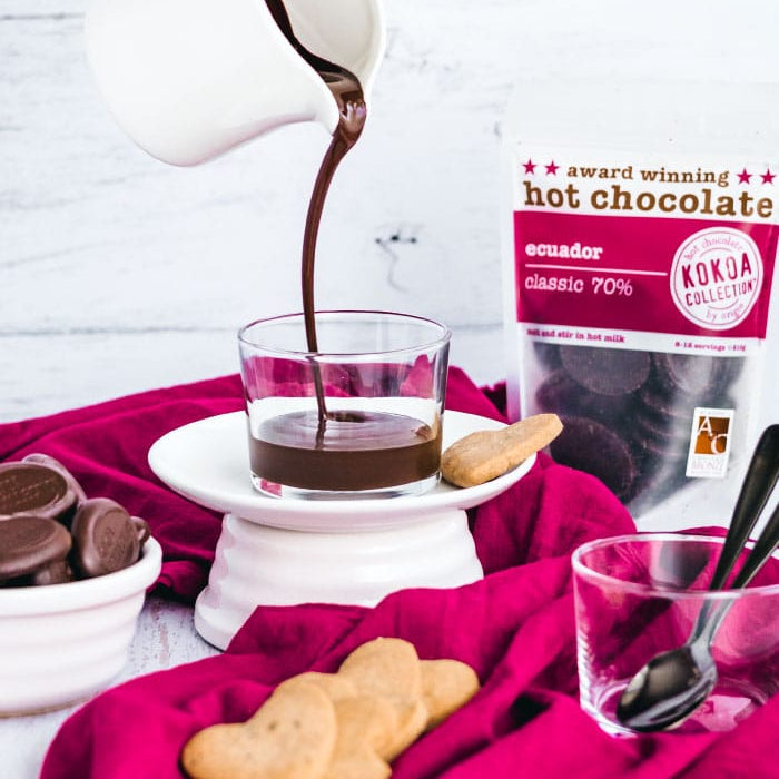 Hot chocolate being poured into a glass with a bag of hot chocolate in the background.