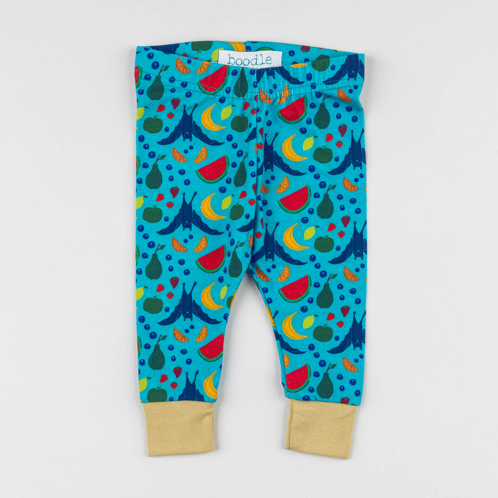 Toddler leggings with a colorful fruit and vegetable print on a turquoise background, featuring beige ribbed ankle cuffs and a white 'boodie' brand label at the waist.