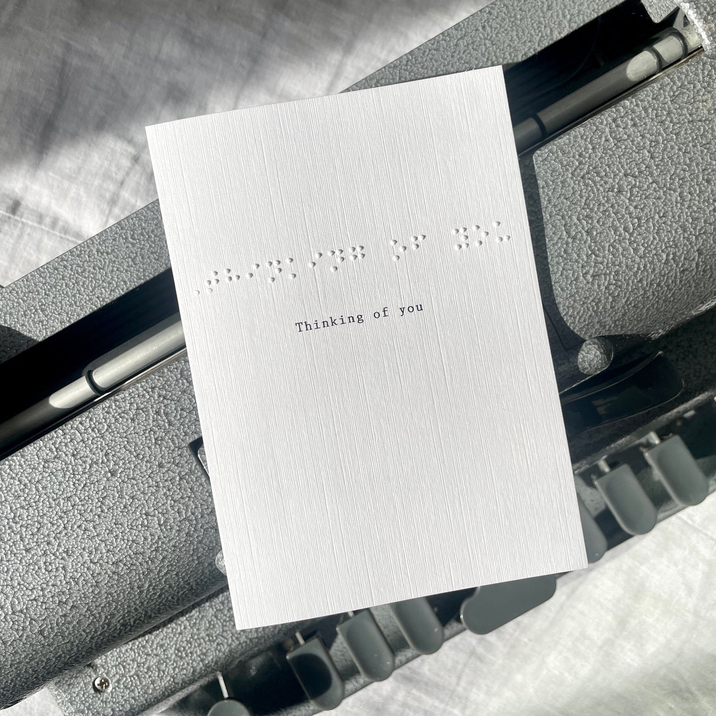 White card with 'Thinking of you' braille text on a textured surface