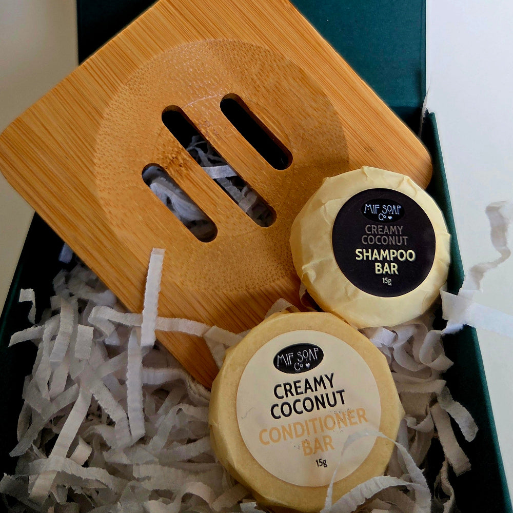 A Mif Soap Co gift set in a dark green box, featuring a bamboo soap dish, a shampoo bar & a conditioner bar, arranged with white paper filler and decorative pearls.