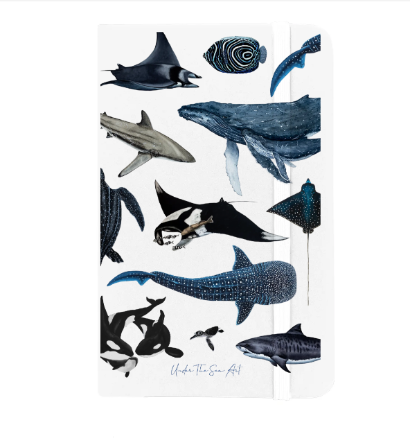 A white hardcover notebook featuring a watercolor-style ocean animal illustration print, including whales, sharks, dolphins, and sea turtles, with a white elastic closure band.