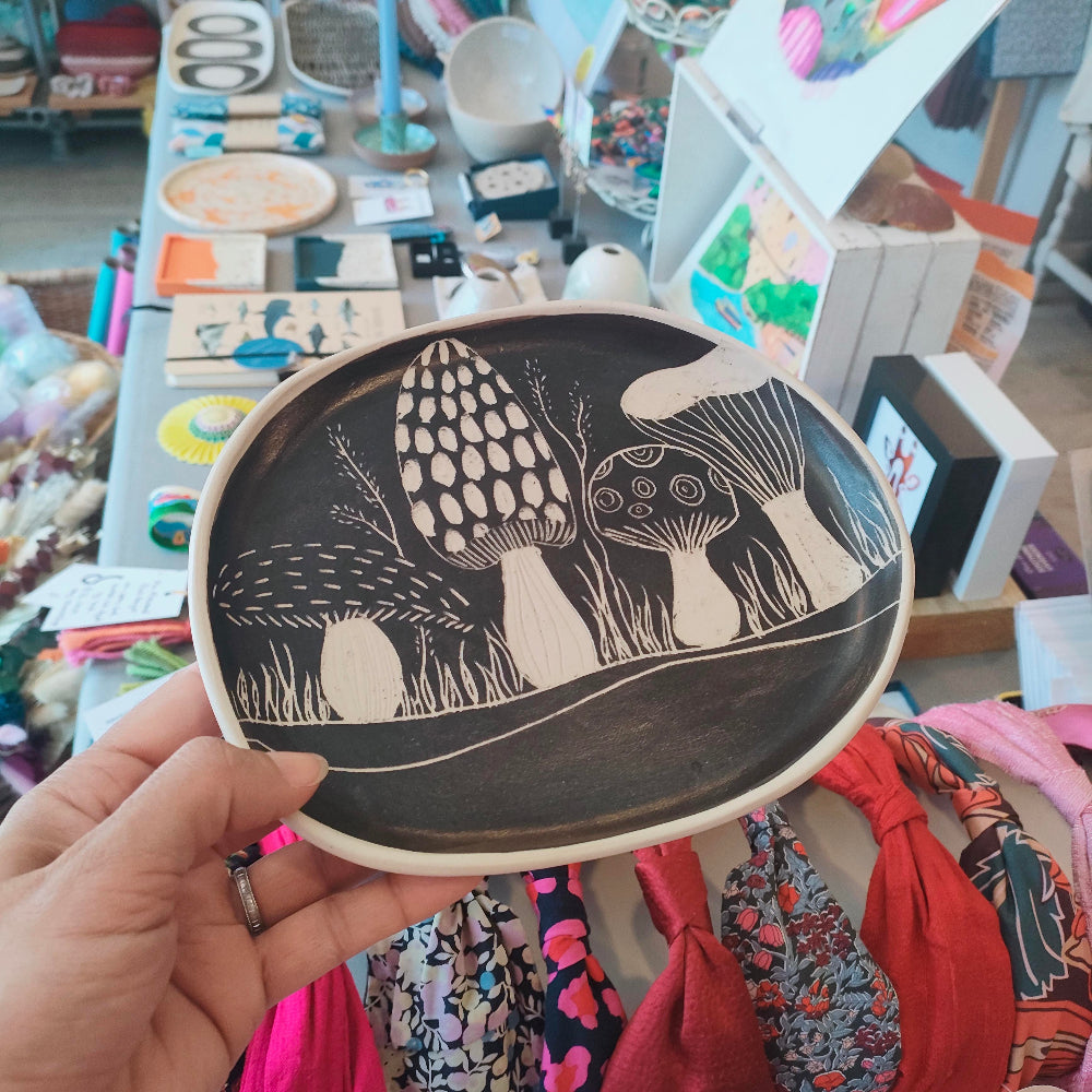 Hand holding a black ceramic plate with white mushroom design in a store setting.