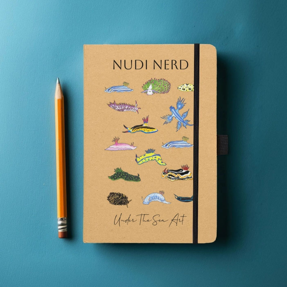 A tan hardcover notebook with a black elastic closure and colorful sea-creature illustrations on the cover, placed on a blue background next to a yellow pencil. The cover reads 'NUDI NERD' and 'Under The Sea Art'.