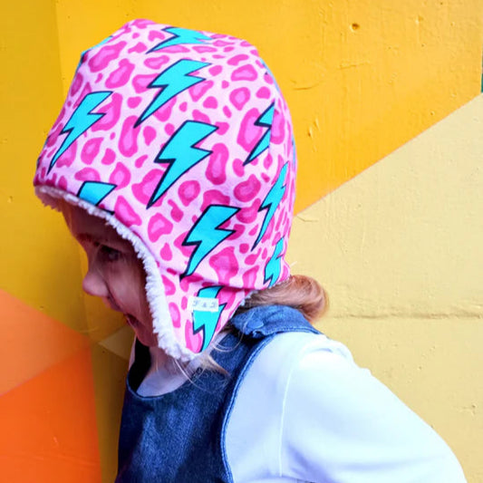 Child wearing a pink helmet with blue lightning bolts against a colorful geometric background