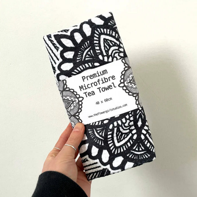 Hand holding a black and white patterned microfiber tea towel with branding on a light background