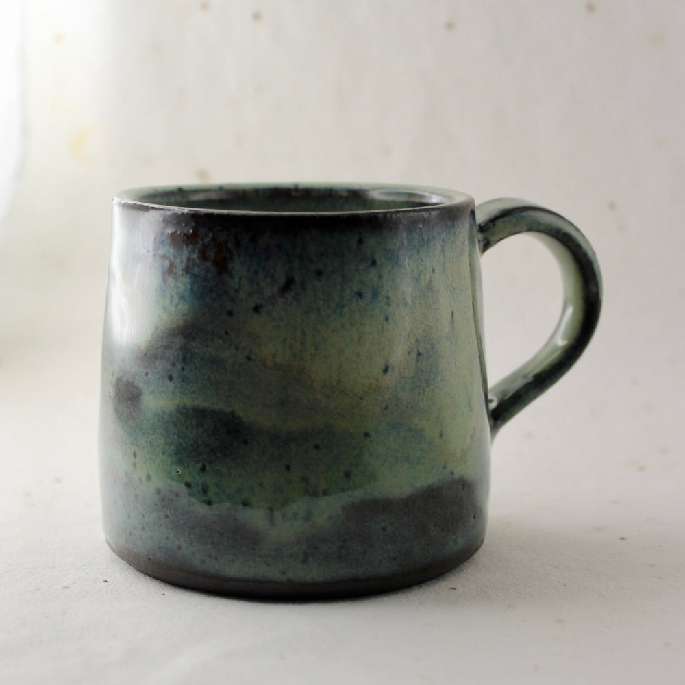 Speckled green and gray ceramic mug on a light background