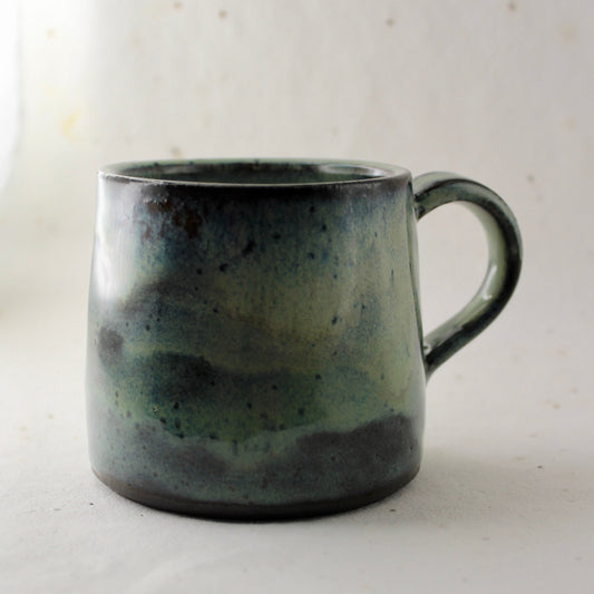 Speckled green and gray ceramic mug on a light background