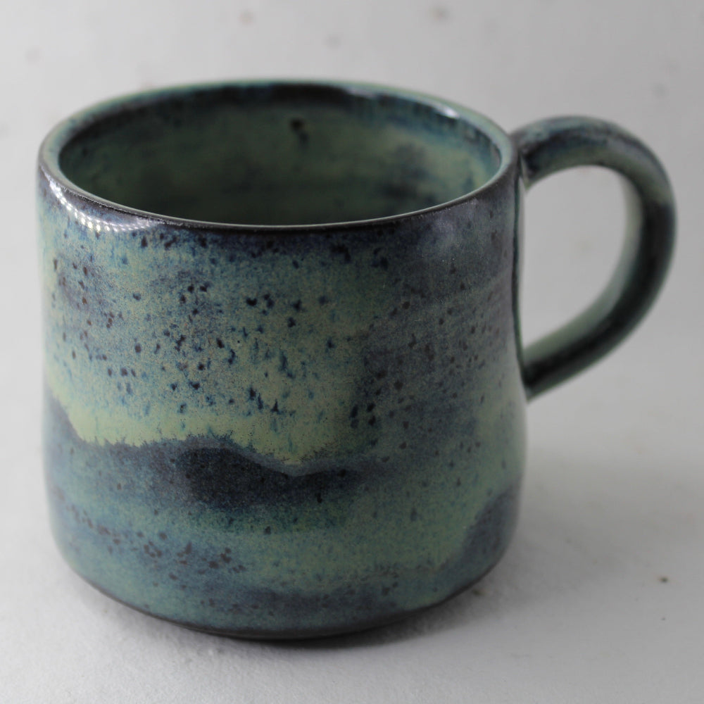 Speckled blue and green ceramic mug on a light gray background